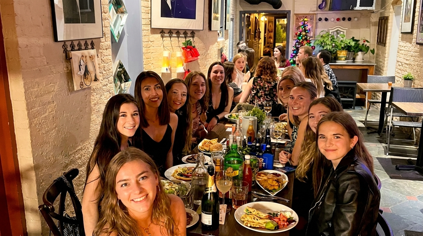 A large group of young women smiling and dining together at a restaurant table filled with food and drinks.