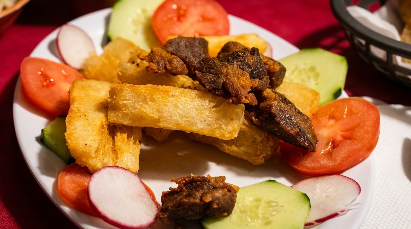 Fried yucca and meat pieces garnished with sliced tomatoes, cucumbers, and radishes on a white plate.