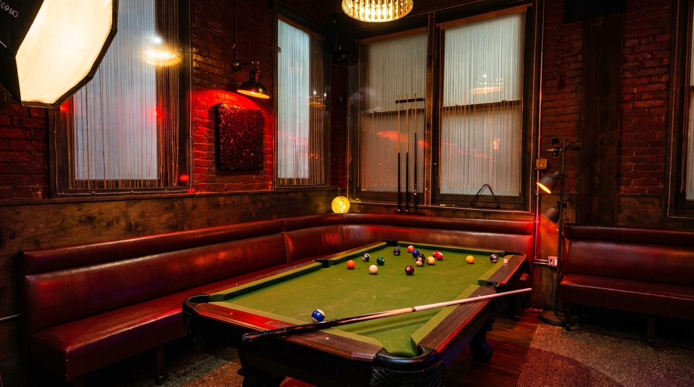 A dimly lit bar area with a pool table, red leather booths, and exposed brick walls.