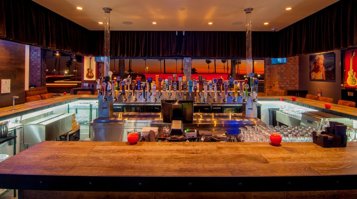 A long, well-lit bar with numerous beer taps and a sunset view through large windows.