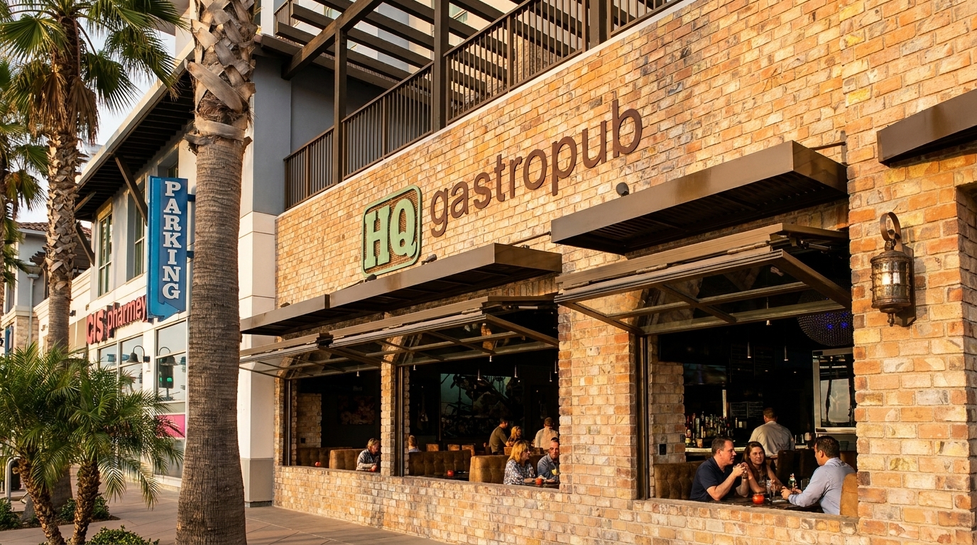 Exterior of HQ Gastropub with open windows, showing patrons dining inside, and palm trees outside.
