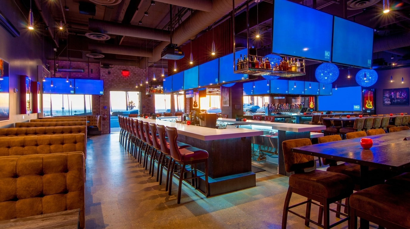 Spacious, modern bar and restaurant with brown booths, long bar with stools, and large blue screens.