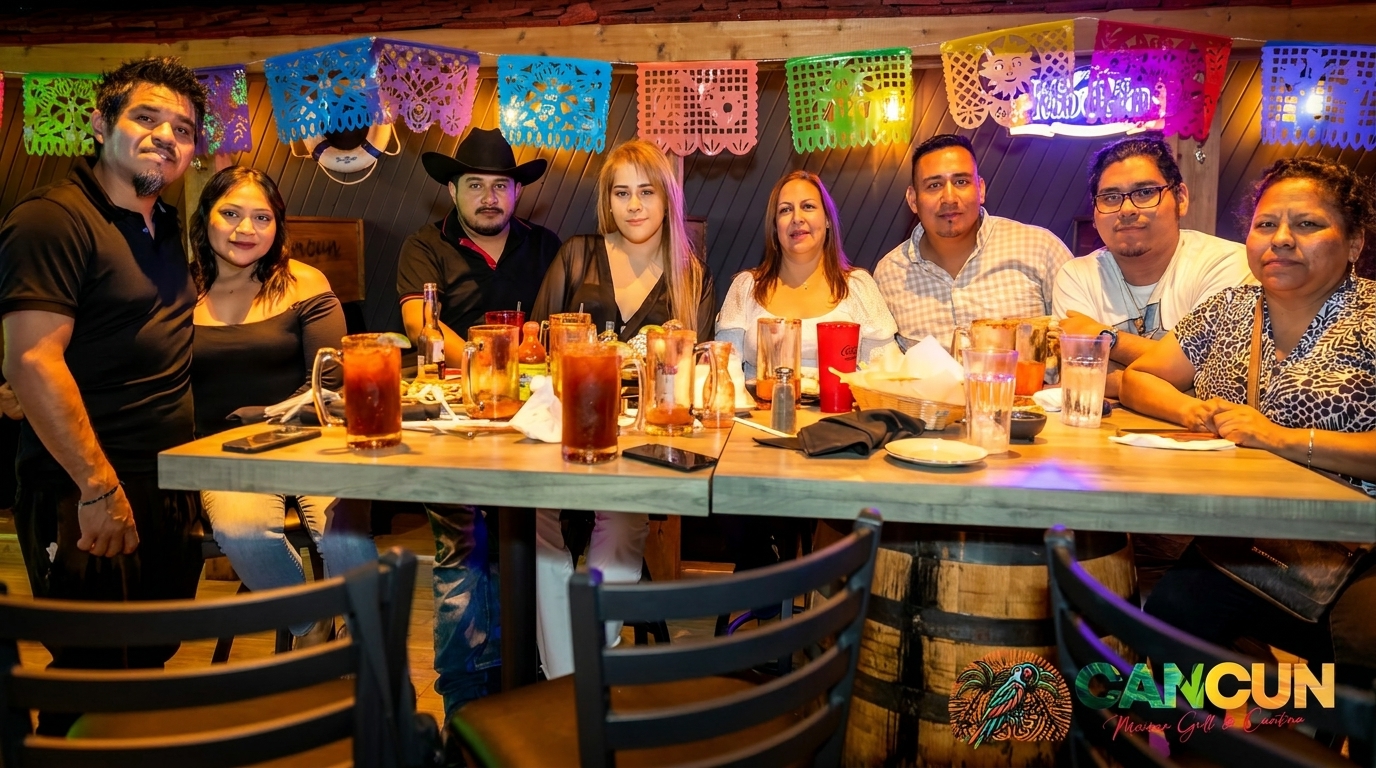 Group of eight people dining at a long table under colorful papel picado decorations.