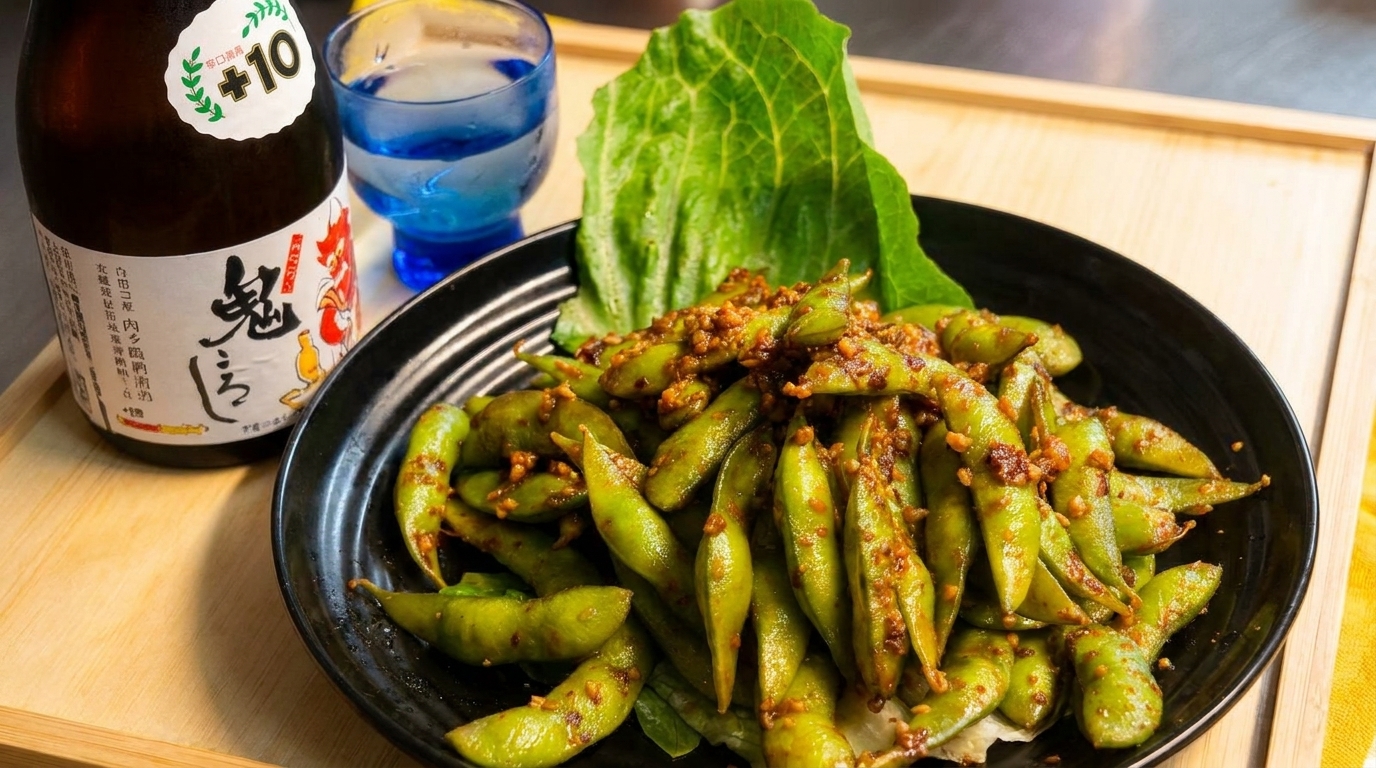 Spicy garlic edamame in a black bowl with a bottle of sake and a blue glass.