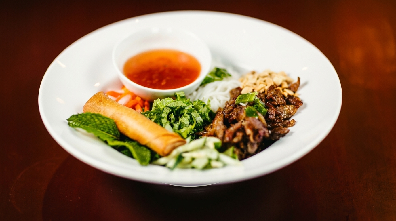 A white bowl of Vietnamese vermicelli with grilled pork, spring roll, and dipping sauce.