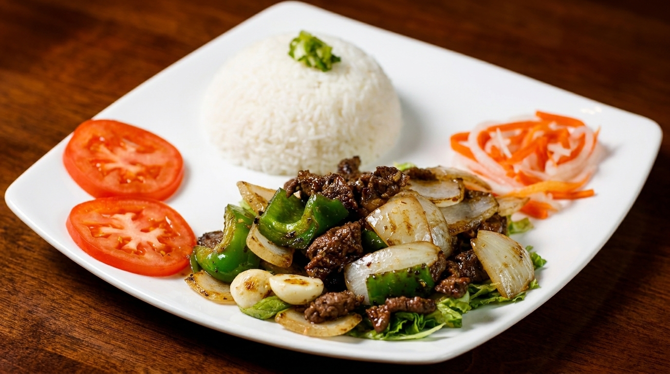 Shaking beef with bell peppers, onions, garlic, rice, tomatoes, and pickled vegetables on a white plate.