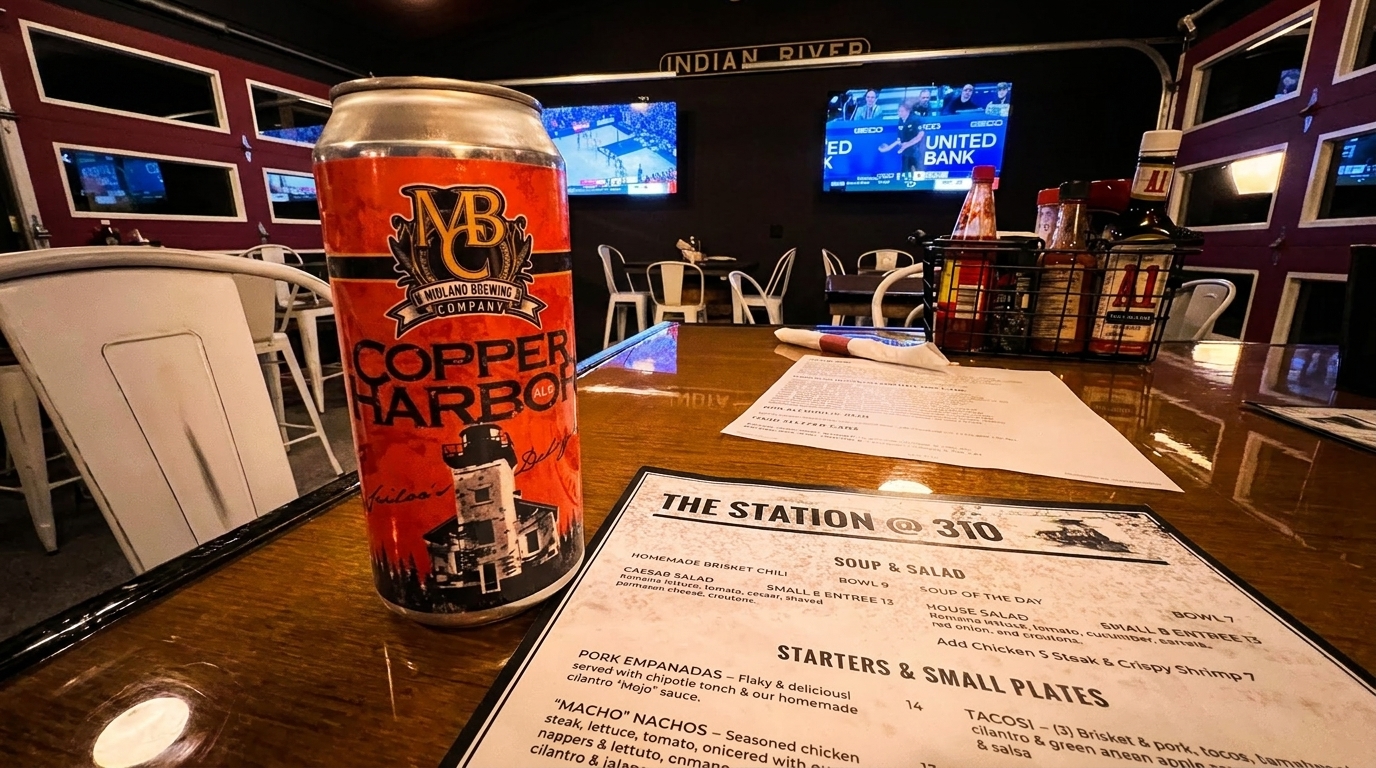 A can of Copper Harbor beer and a menu on a wooden table inside a restaurant with TVs in the background.