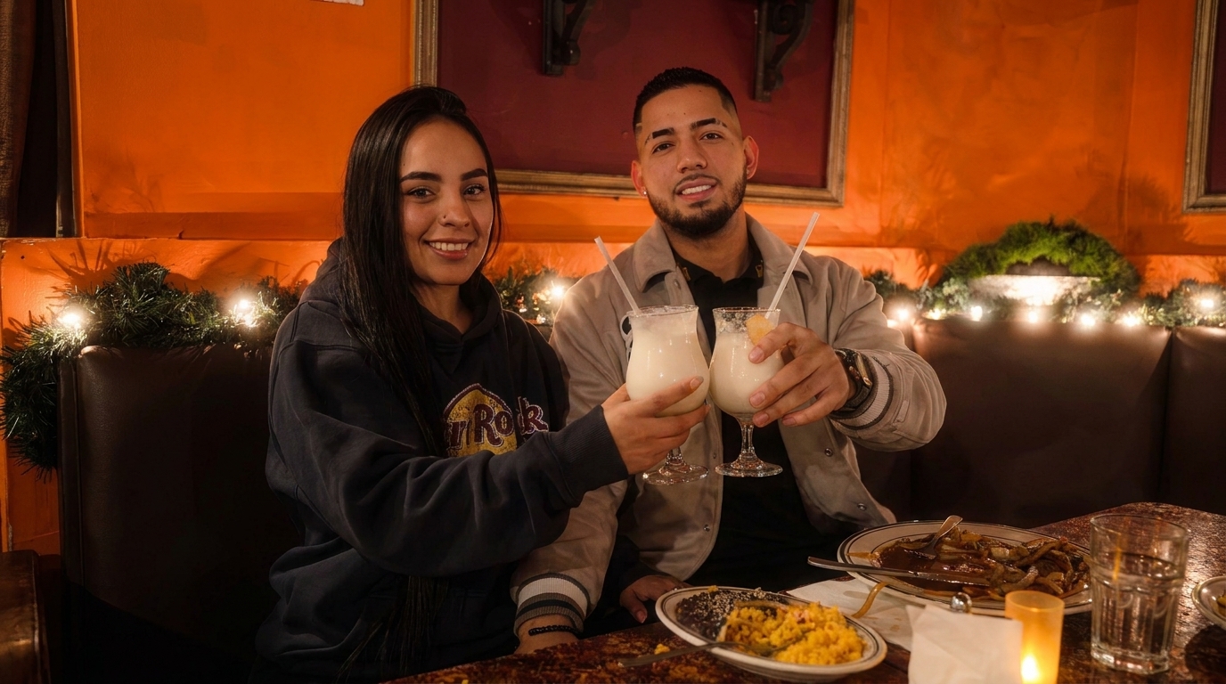 A smiling couple toasts with frozen drinks at a restaurant table with food and festive decor.