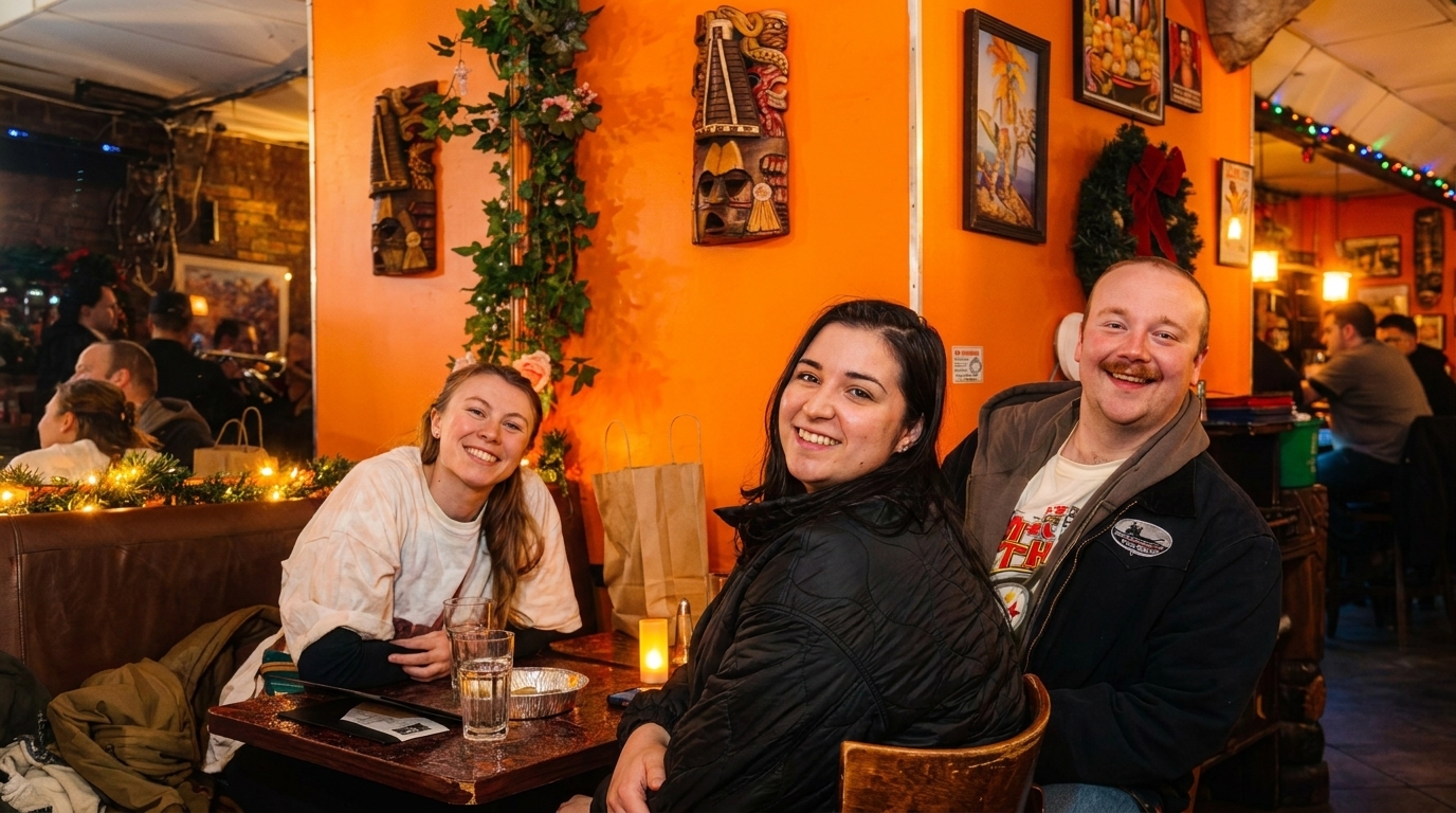 Three smiling people sitting at a table in a restaurant with orange walls and festive decor.