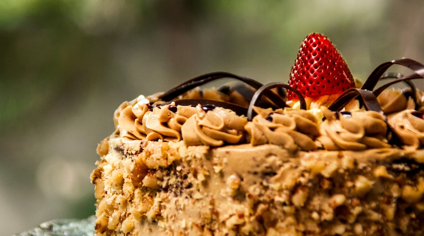 Close-up of a cake with nuts, coffee frosting, chocolate curls, and a single strawberry on top.