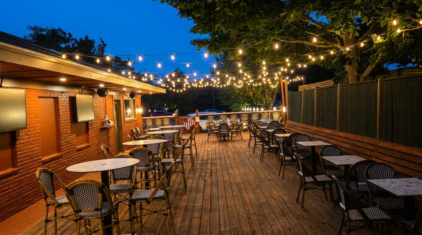 An outdoor restaurant patio at dusk, with string lights illuminating numerous tables and chairs.