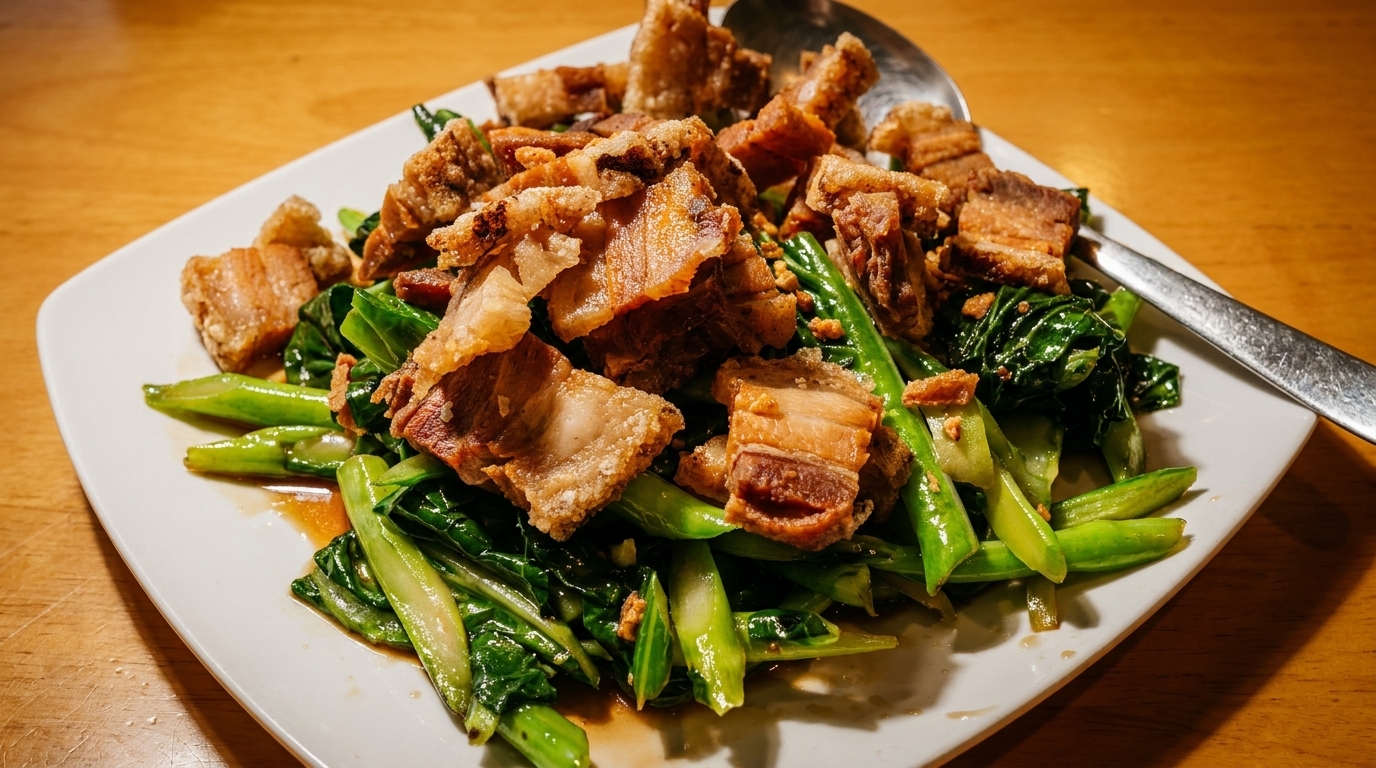 Crispy pork belly and stir-fried Chinese broccoli on a white plate with a spoon.