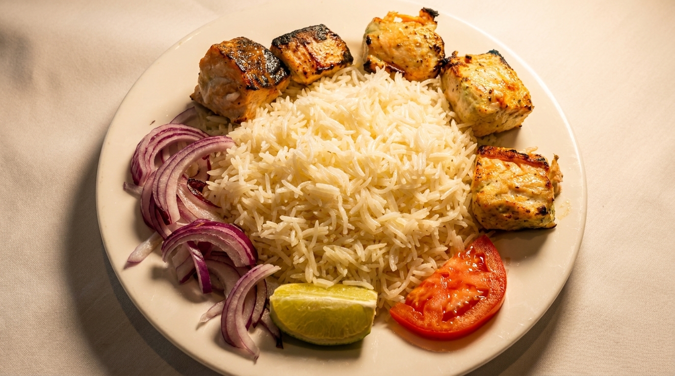 Grilled salmon pieces, white rice, red onion, tomato slice, and lime wedge on a white plate.