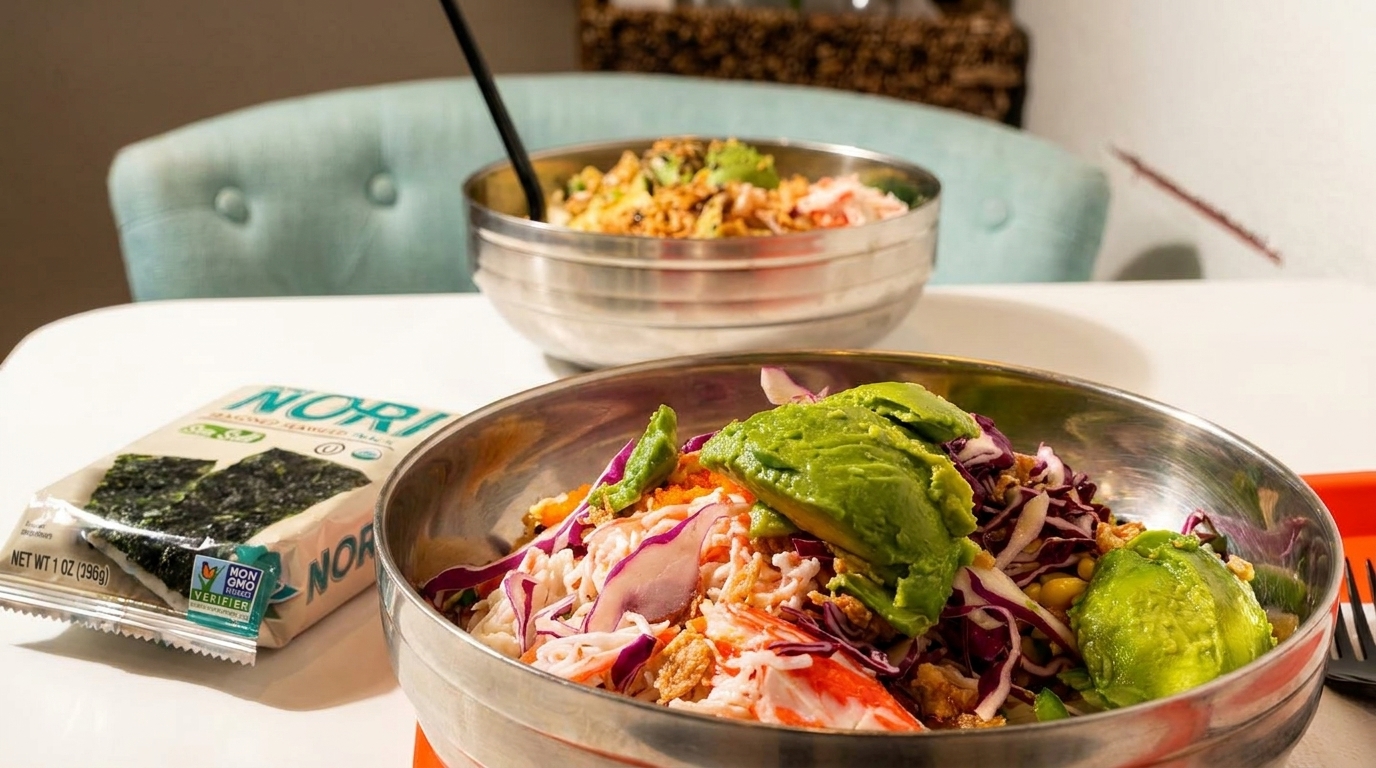 Two poke bowls with avocado, crab, and red cabbage, plus a package of nori on a white table.