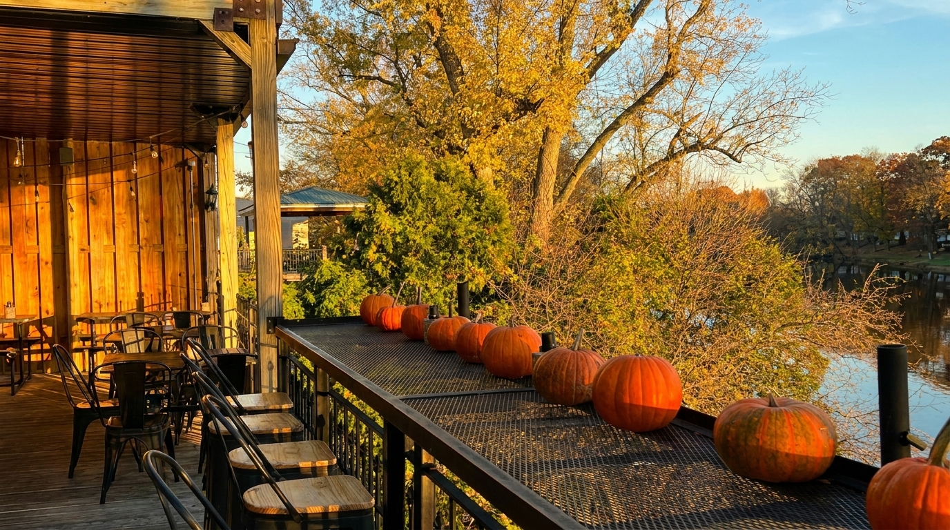 Outdoor restaurant patio with pumpkins on the railing, overlooking a river and autumn trees.