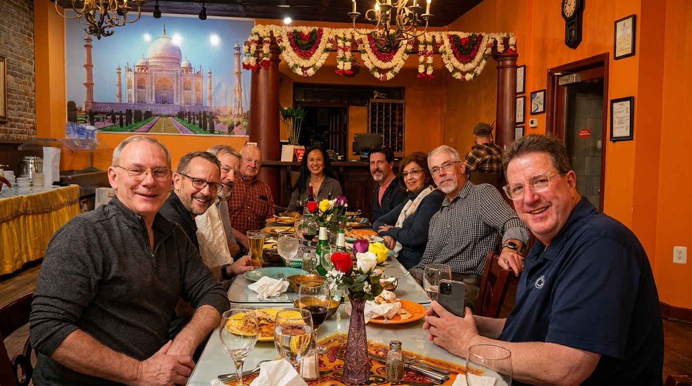 A group of friends smiling and dining at a long table in an Indian restaurant.