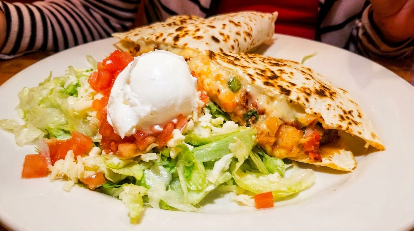Two cheesy quesadillas with chicken, salsa, sour cream, and a side salad on a white plate.
