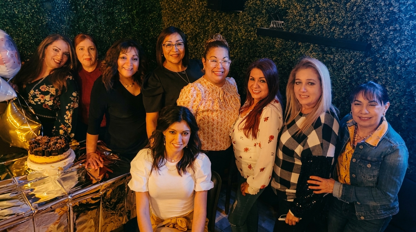 Nine women smiling for a group photo at a celebration with a cake and balloons.