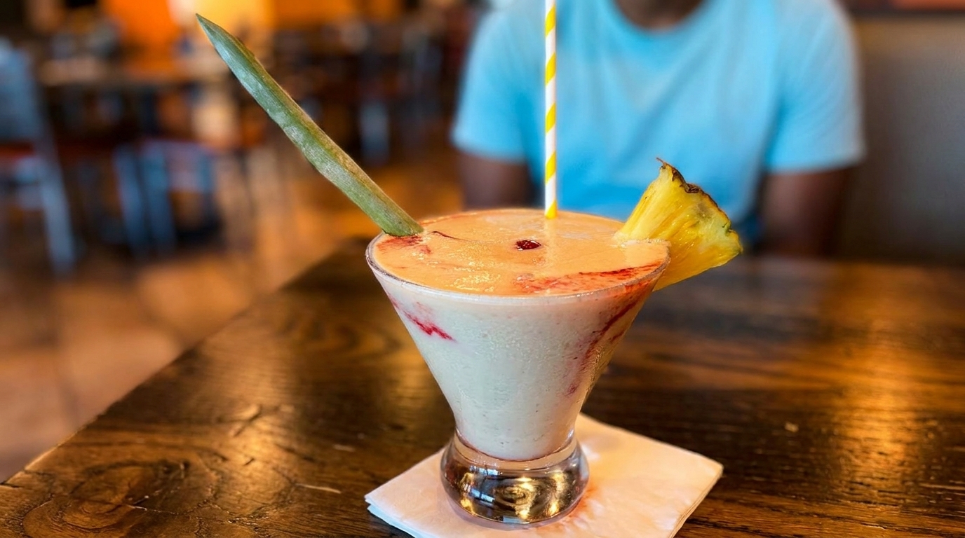 Tropical drink with pineapple and a green garnish on a wooden table, with a person in the background.