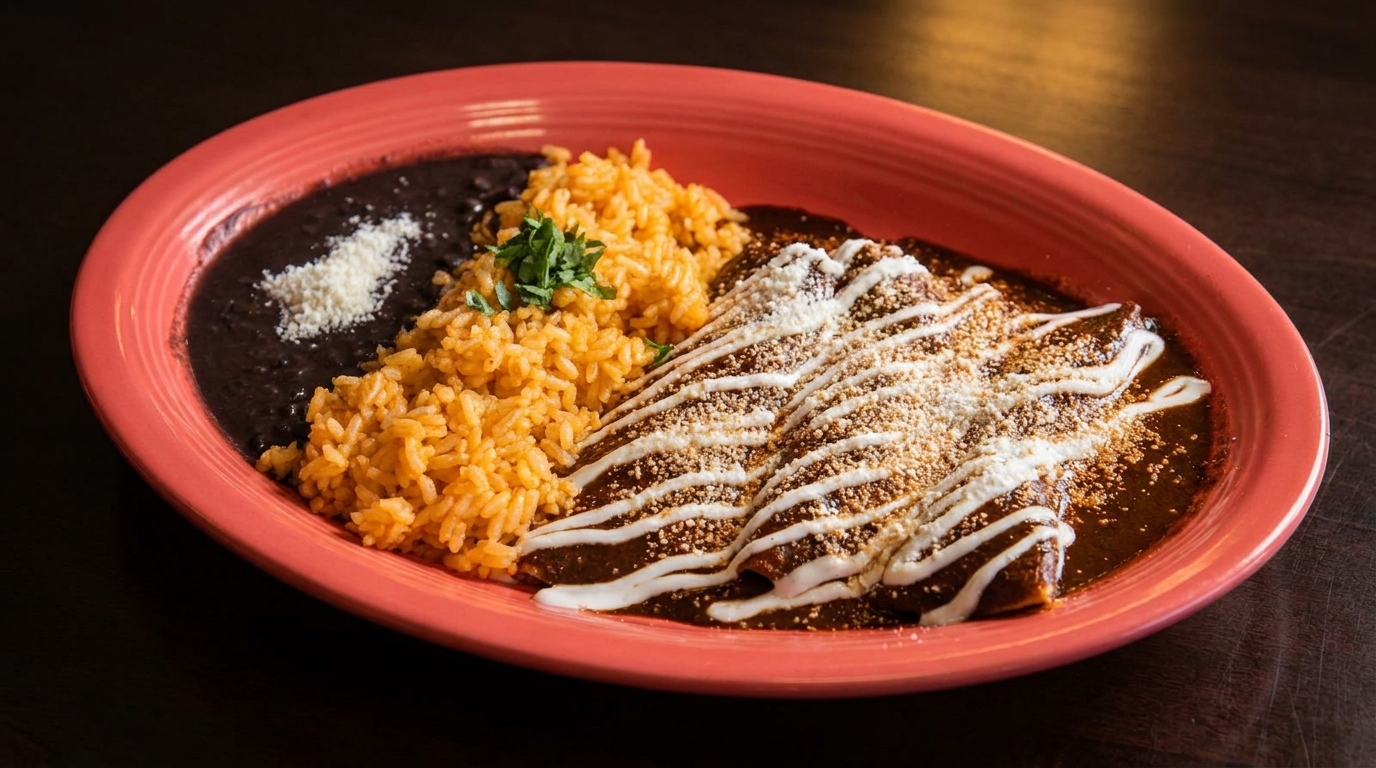 Three enchiladas covered in dark sauce, crema, and cheese, served with rice and black beans.
