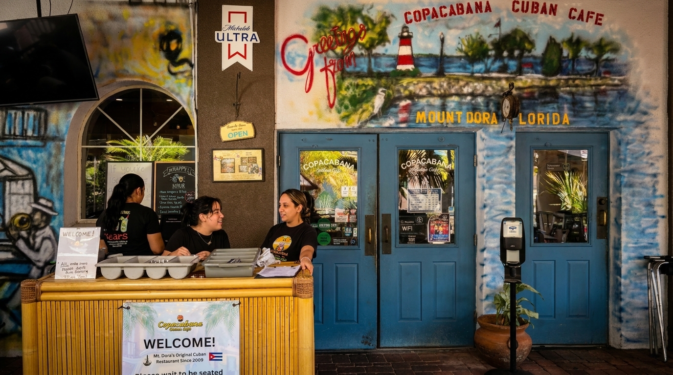 Three women at a host stand outside Copacabana Cuban Cafe, with a colorful mural above blue doors.