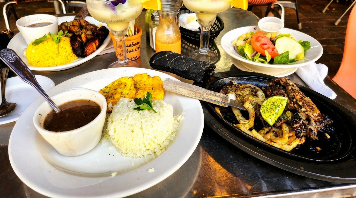 Table laden with Cuban dishes: yellow rice, black beans, plantains, grilled meat, and margaritas.