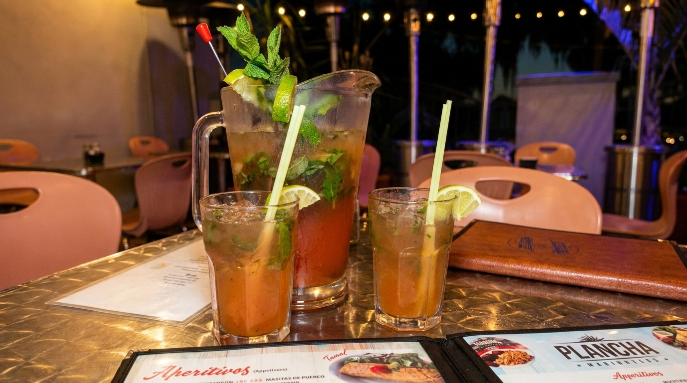 Pitcher and two glasses of mojitos with lime and mint on a restaurant table at night.