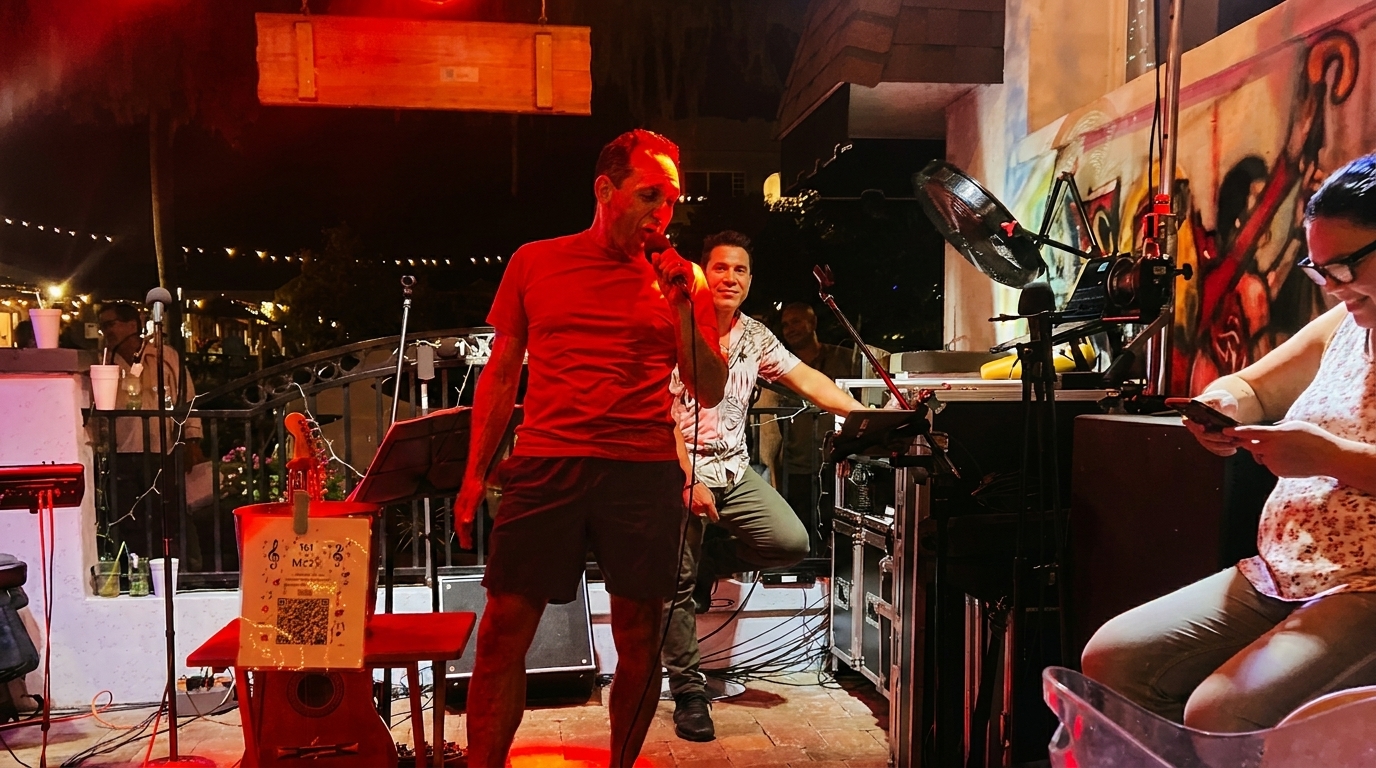 A man sings into a microphone on an outdoor stage at night, illuminated by red light.