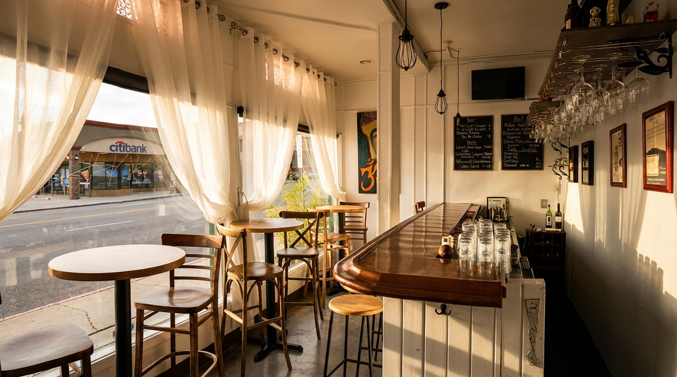 Sunny restaurant interior with a long wooden bar, high-top tables, and sheer white curtains by the window.