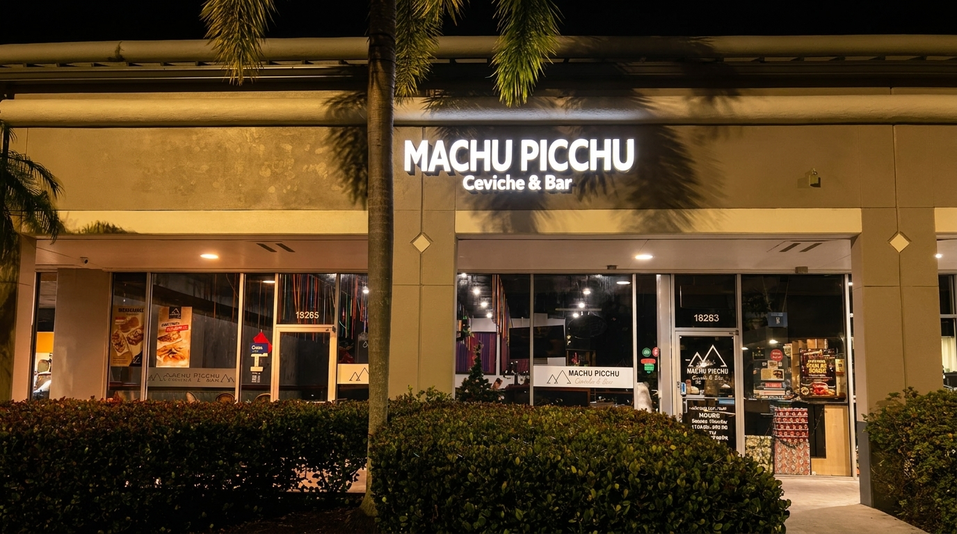 Exterior of Machu Picchu Ceviche & Bar at night, with illuminated sign and palm trees.