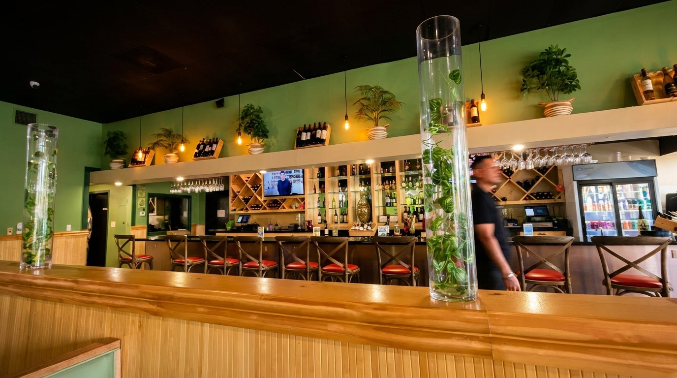 A restaurant bar with green walls, wooden paneling, bar stools, and a bartender in motion.